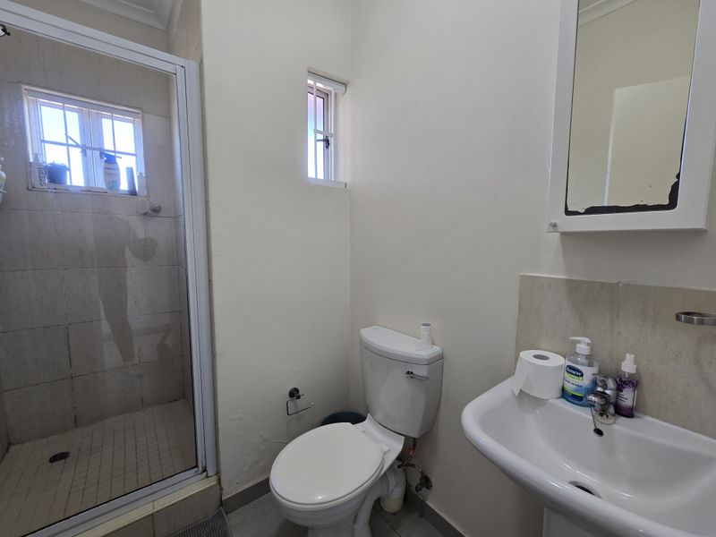 A functional bathroom featuring a shower enclosure, pedestal sink, and wall-mounted medicine cabinet with a tiled shower base.