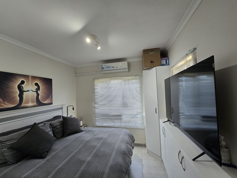A well-maintained bedroom featuring tiled flooring, a built-in wardrobe, venetian blinds, and a wall-mounted air conditioning unit.