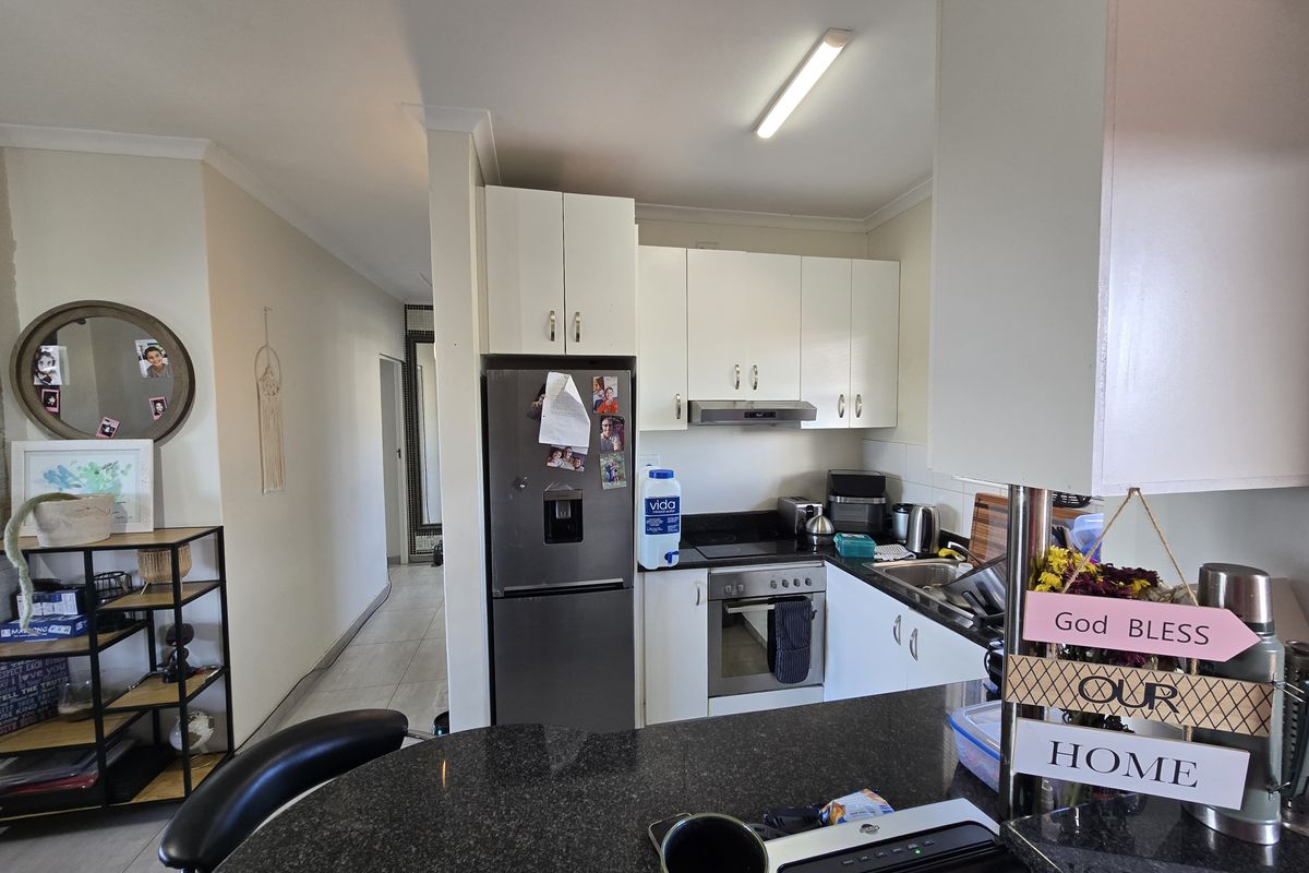 Compact kitchen featuring white cabinetry, granite countertops, and integrated stainless steel appliances, opening into a tiled hallway area.