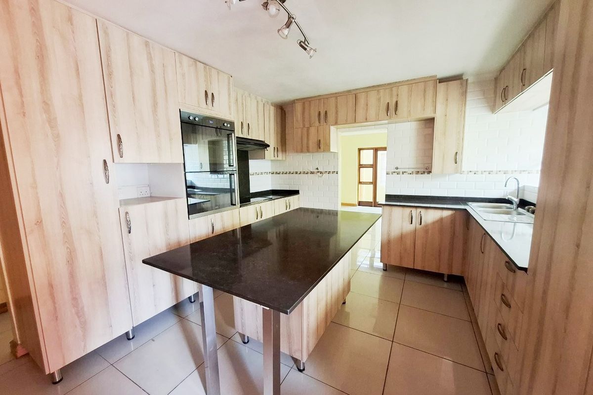 A spacious kitchen featuring light wood cabinetry, dark granite countertops, a central island, built-in oven, and tiled flooring.
