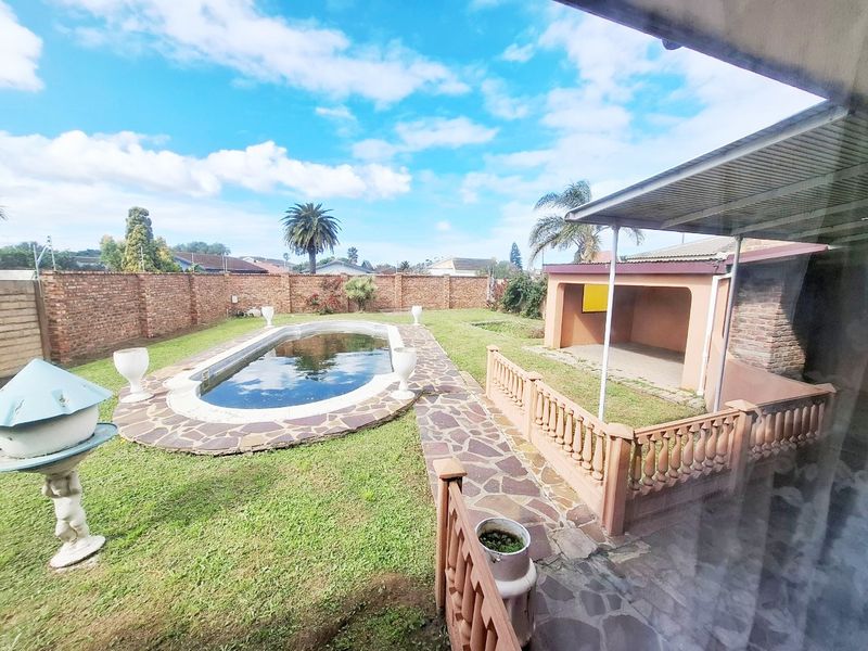 Rear garden featuring a swimming pool, brick boundary walls, and a covered patio area with stone paving.