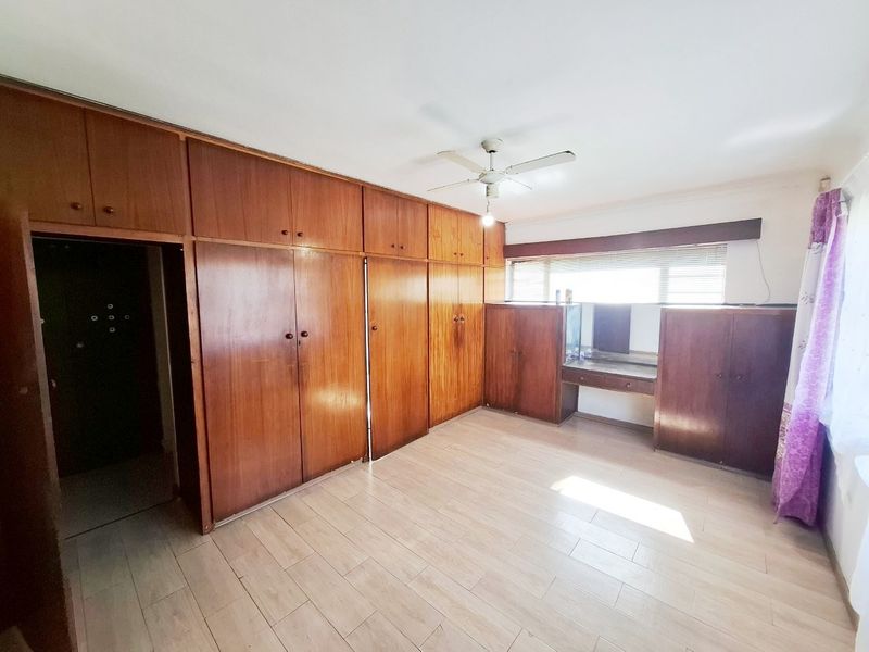 A spacious bedroom featuring extensive built-in wooden cabinetry, a ceiling fan, and light-toned tiled flooring with natural light from the window.