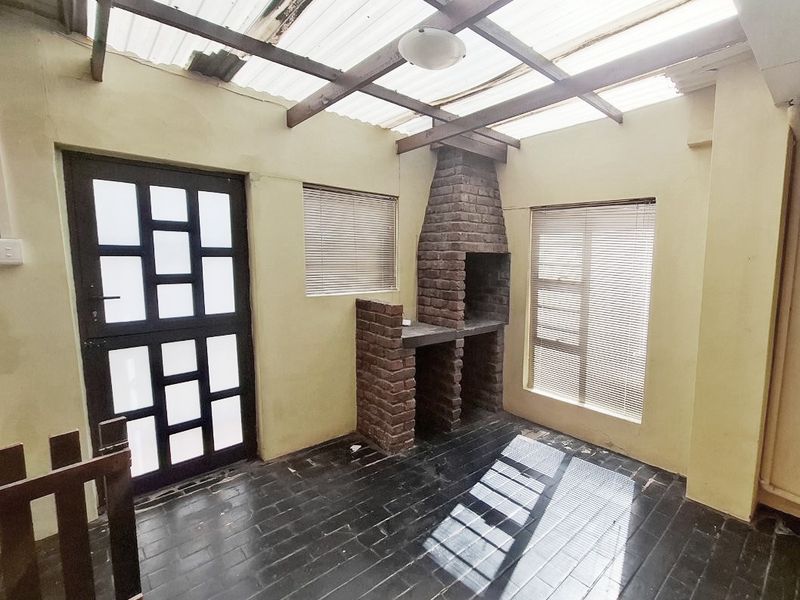 Covered patio area featuring a built-in brick braai, tiled flooring, and a translucent roof structure, offering a versatile space for outdoor entertaining.