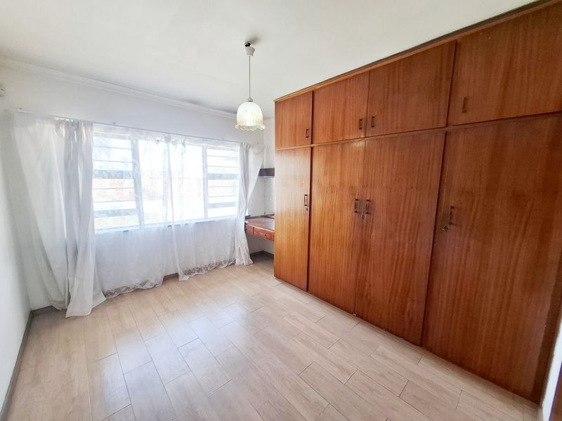A bright, empty bedroom featuring extensive built-in wooden cabinetry, a matching vanity desk, and light-toned laminate flooring.