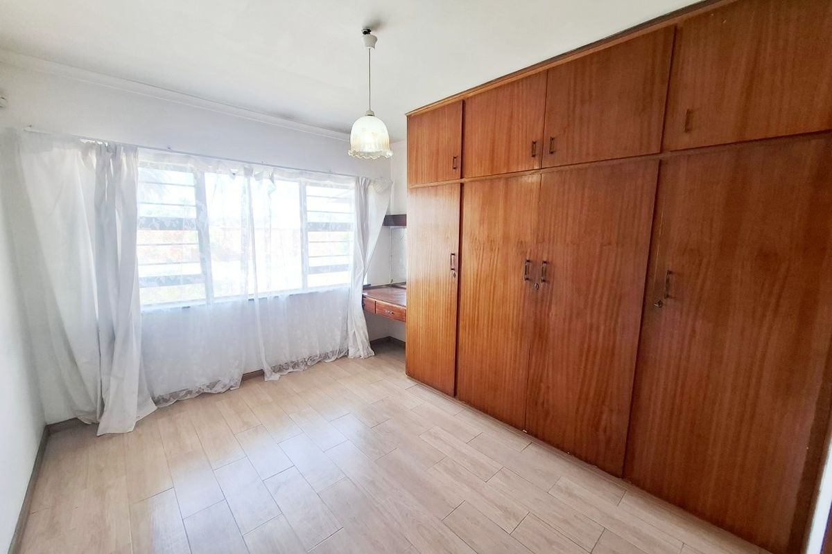 A bright, empty bedroom featuring extensive built-in wooden cabinetry, a matching vanity desk, and light-toned laminate flooring.
