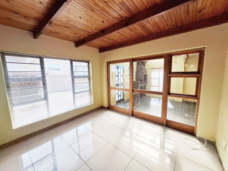 Bright and spacious living area featuring a warm timber beam ceiling, large windows, and sliding glass doors leading to an outdoor patio space.