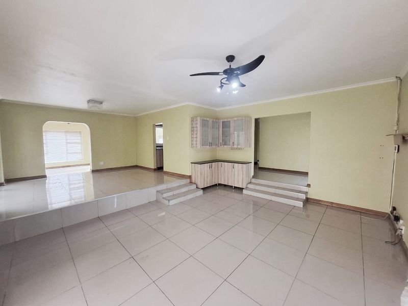 Spacious open-plan living area featuring tiled flooring, a raised platform section, and built-in cabinetry, offering a versatile layout for modern living.