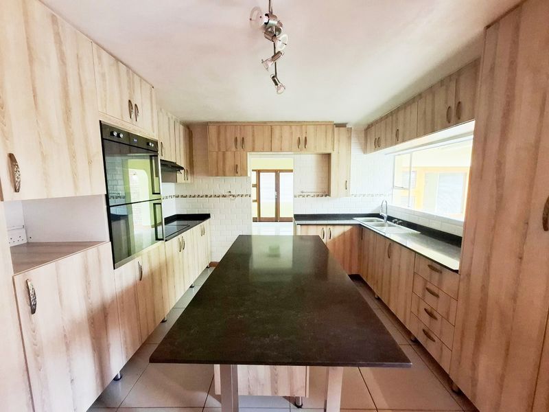 A spacious, modern kitchen featuring light wood cabinetry, dark stone countertops, a central island, and integrated appliances including a double wall oven.