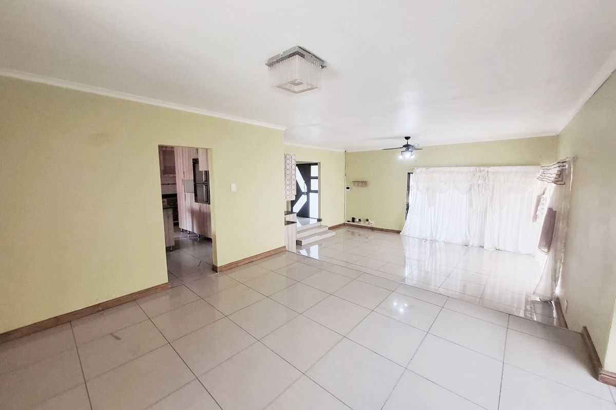Spacious, open-plan living area featuring neutral tiled flooring, a ceiling fan, and direct access to adjacent rooms.