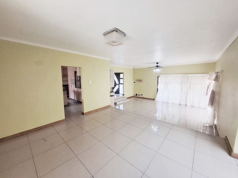 Spacious, open-plan living area featuring neutral tiled flooring, a ceiling fan, and direct access to adjacent rooms.