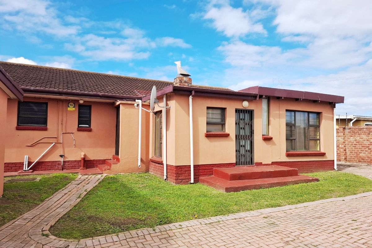 Rear view of the house featuring a tiled roof, brick chimney, security gate, and paved garden area.