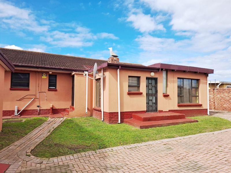 Rear view of the house featuring a tiled roof, brick chimney, security gate, and paved garden area.
