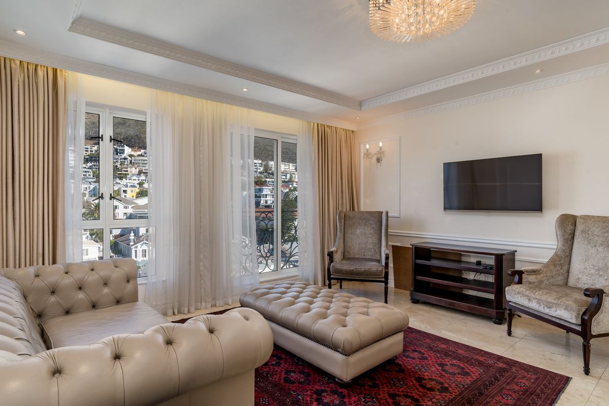 Elegant living room featuring crown molding, wainscoting, stone flooring, and large windows with balcony access, offering a bright and sophisticated atmosphere.