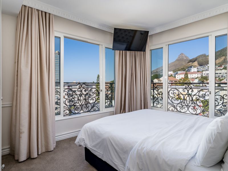 A bright bedroom featuring large windows with wrought iron railings, crown molding, and scenic mountain and city views.