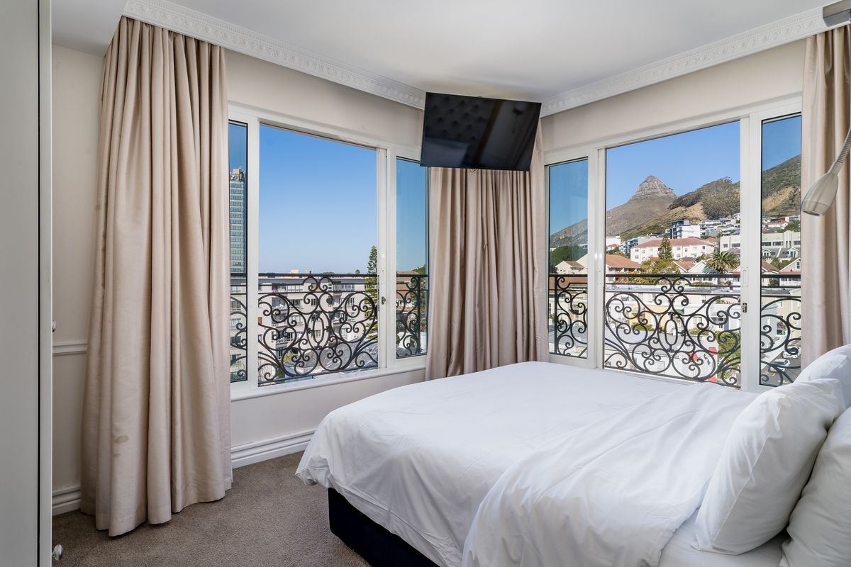 A bright bedroom featuring large windows with wrought iron railings, crown molding, and scenic mountain and city views.