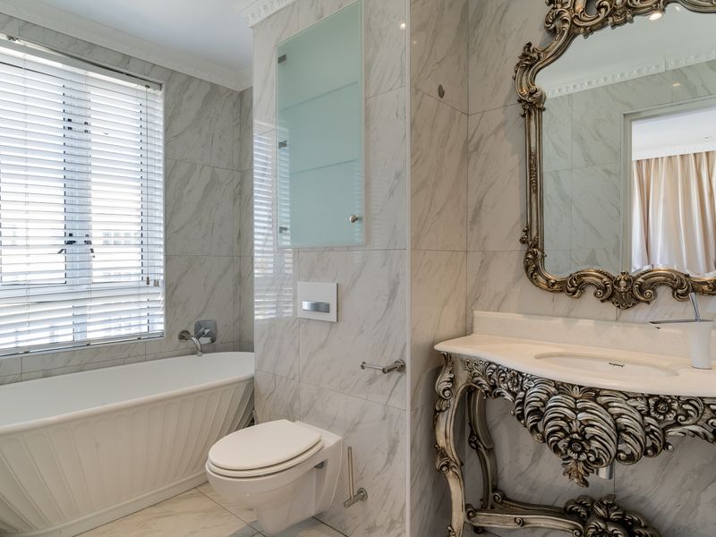 A luxurious bathroom featuring marble wall and floor tiles, a freestanding bathtub, a wall-mounted toilet, and an ornate vanity basin.