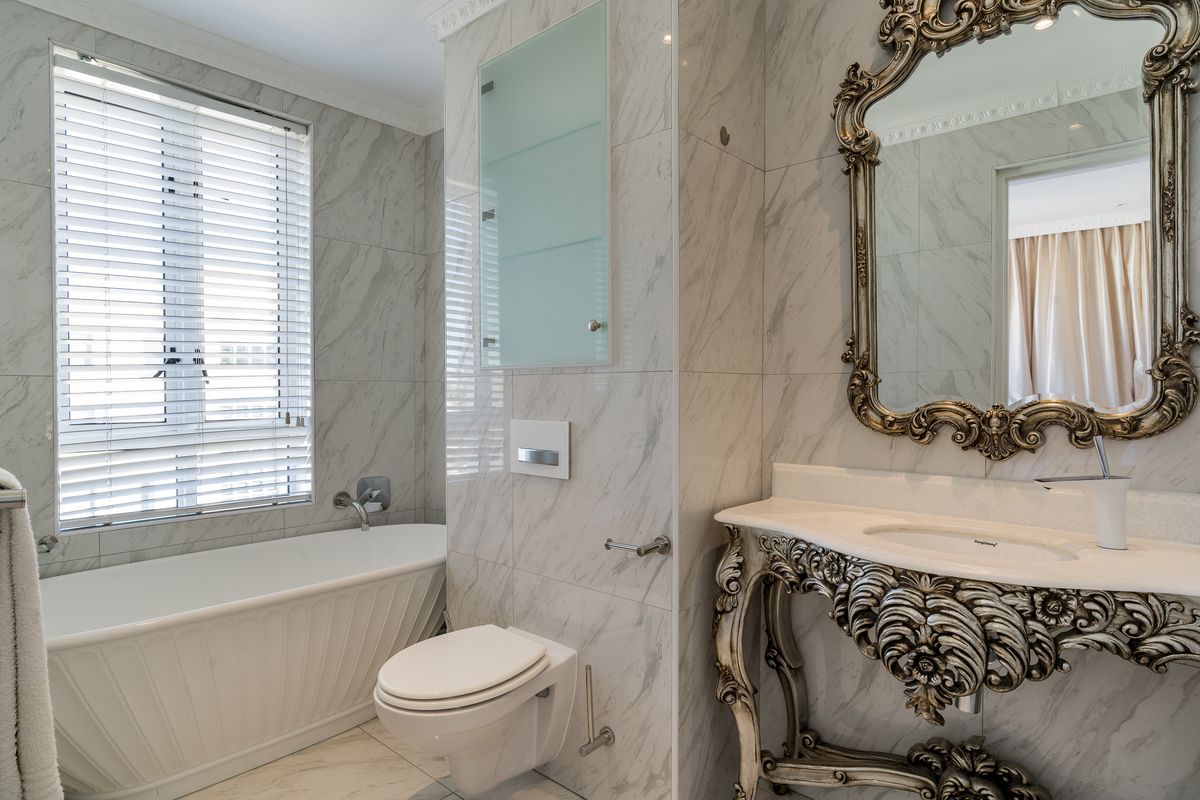 A luxurious bathroom featuring marble wall and floor tiles, a freestanding bathtub, a wall-mounted toilet, and an ornate vanity basin.