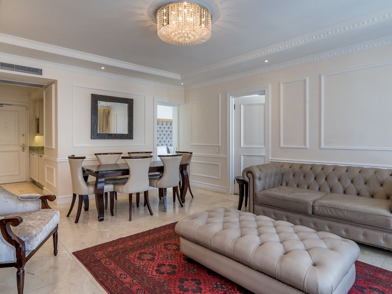 Elegant open-plan living and dining area featuring classic wainscoting, intricate crown molding, polished marble flooring, and a sophisticated crystal chandelier.