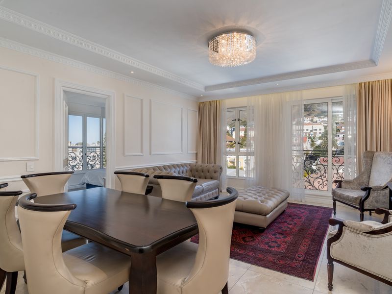 Elegant open-plan living and dining area featuring classic wainscoting, crown molding, stone flooring, and access to a balcony with wrought iron railings.