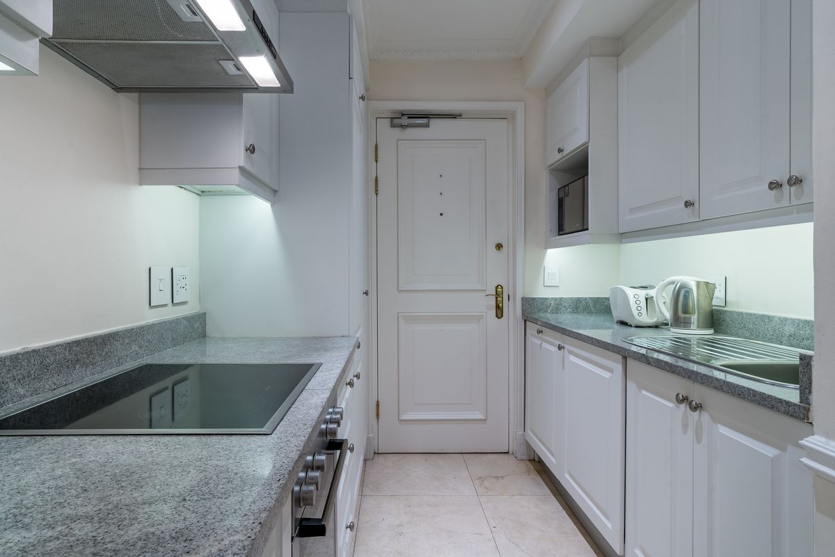 A compact, well-maintained kitchen featuring granite countertops, white cabinetry, an integrated electric hob, and built-in oven with modern under-cabinet lighting.