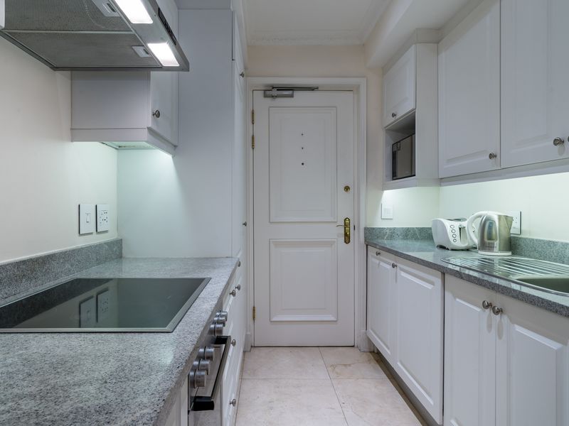 A compact, well-maintained kitchen featuring granite countertops, white cabinetry, an integrated electric hob, and built-in oven with modern under-cabinet lighting.