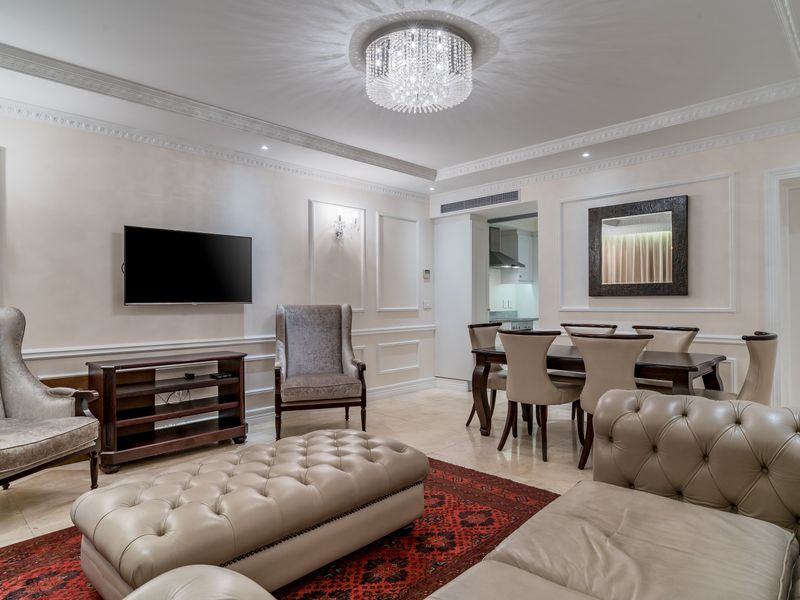 Elegant open-plan living and dining area featuring sophisticated wainscoting, crown molding, stone flooring, and a prominent crystal chandelier.