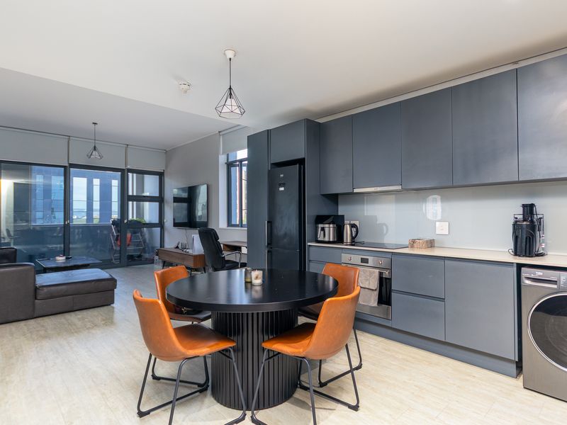 Modern open-plan apartment featuring a sleek grey kitchen with integrated appliances, flowing into a living area with access to a private balcony.