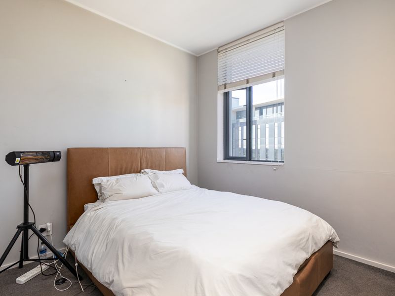A well-lit bedroom featuring neutral wall tones, carpeted flooring, and a window fitted with venetian blinds.