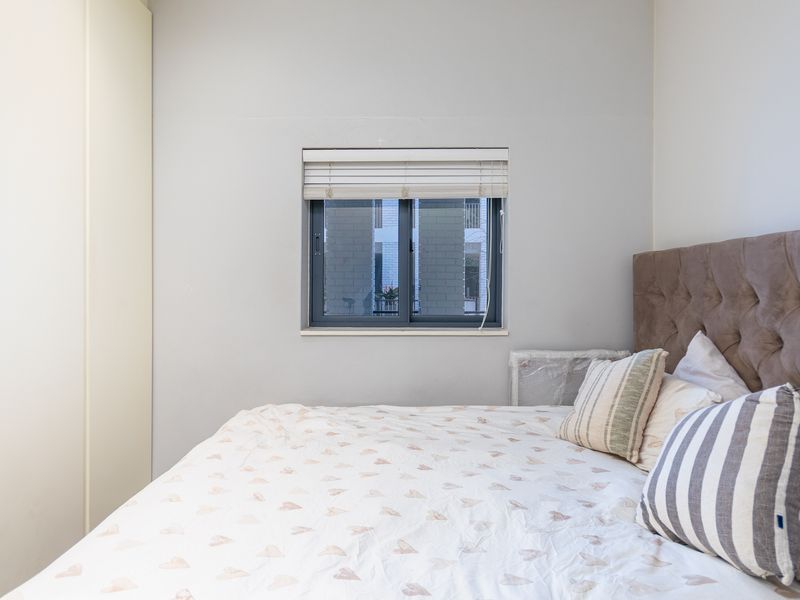 A well-maintained bedroom featuring a built-in wardrobe, neutral wall finishes, and a sliding window with a fitted venetian blind.