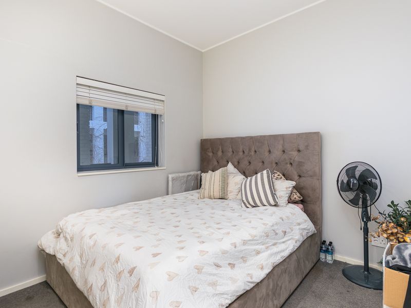 A well-maintained bedroom featuring neutral wall tones, carpeted flooring, and a window fitted with venetian blinds.
