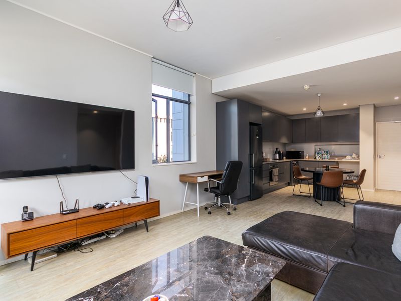 Modern open-plan living area featuring a sleek kitchen with dark cabinetry and integrated appliances, flowing into a comfortable lounge space.