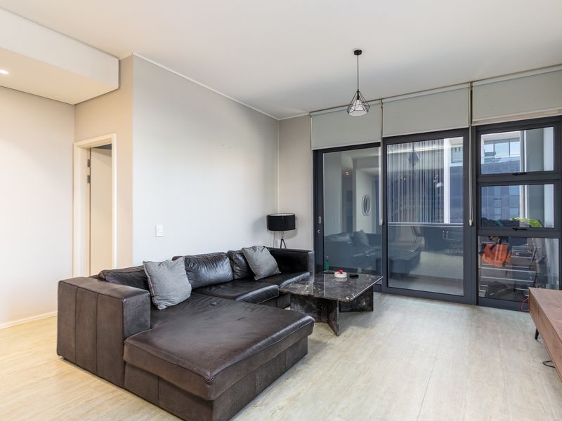 Modern living room featuring light laminate flooring, recessed lighting, and large sliding glass doors providing access to the balcony.