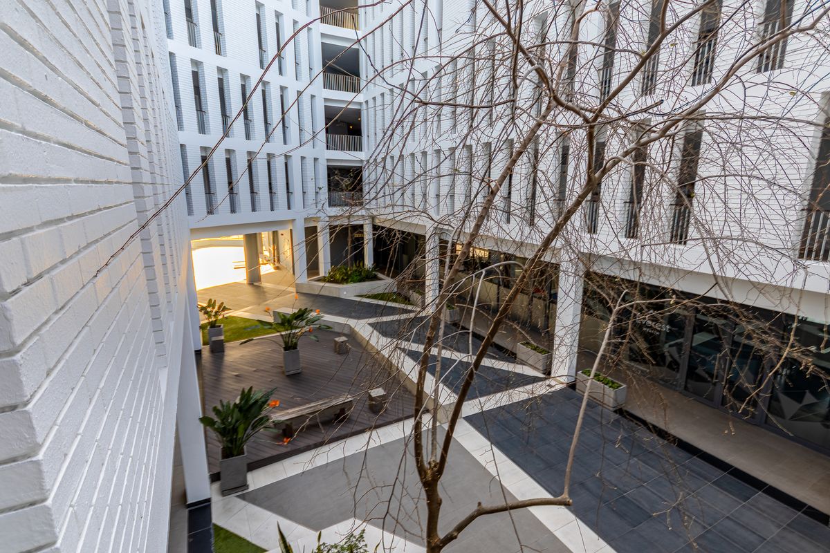 A modern apartment complex courtyard featuring a mix of paved walkways, timber decking, and multi-story white brick architectural facades.