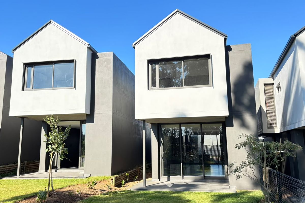 Rear view of modern two-story residential units featuring clean architectural lines, sliding glass doors, and private patio areas overlooking a landscaped lawn.