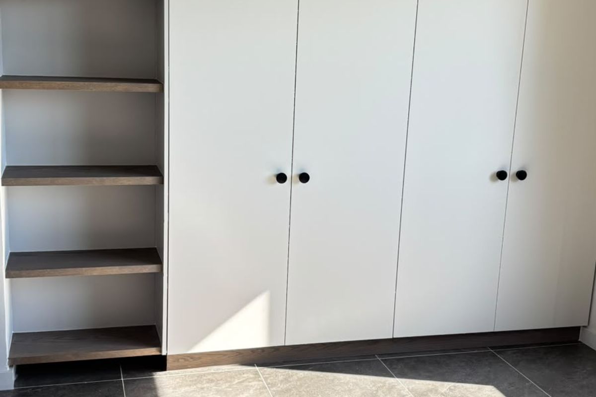 A modern bedroom featuring sleek built-in cupboards with integrated open shelving and contemporary dark grey tiled flooring.