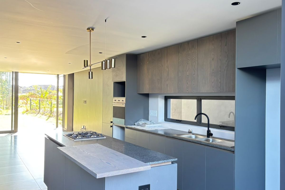 Modern open-plan kitchen featuring sleek dark cabinetry, stone countertops, a central island with a gas hob, and integrated appliances.