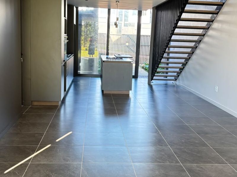 Modern open-plan living and kitchen area featuring sleek cabinetry, a central island, tiled flooring, and a contemporary staircase leading to the upper level.