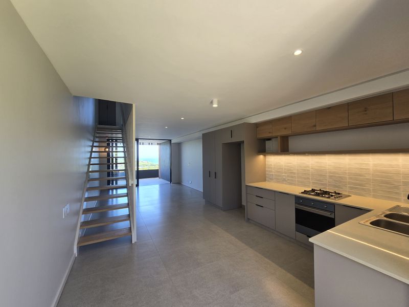 Modern open-plan kitchen and living area featuring sleek cabinetry, integrated appliances, tiled flooring, and a staircase leading to the upper level.