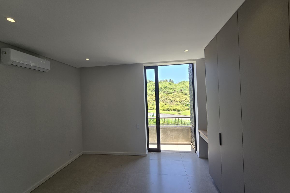 Modern, empty bedroom featuring built-in cupboards, air conditioning, tiled flooring, and direct access to a private balcony with scenic views.