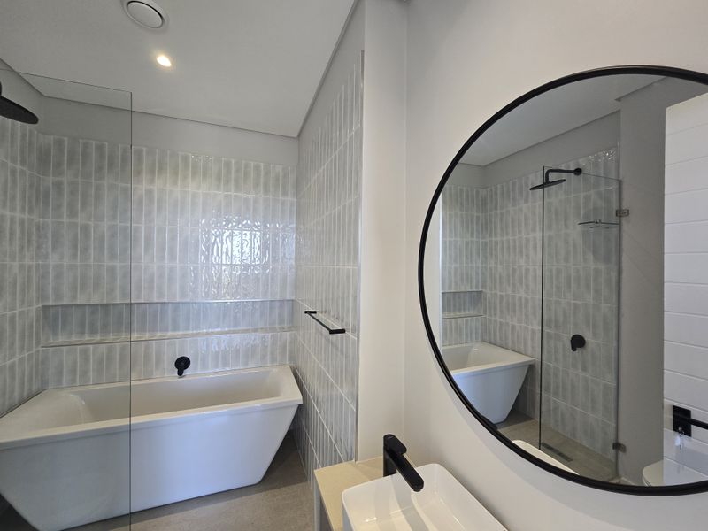 Modern bathroom featuring a freestanding bathtub, walk-in shower with glass screen, vessel sink, and contemporary black matte fixtures with stylish wall tiling.