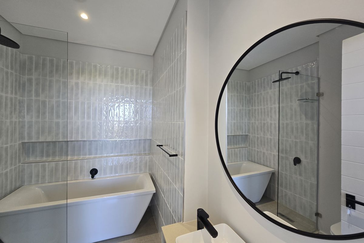 Modern bathroom featuring a freestanding bathtub, walk-in shower with glass screen, vessel sink, and contemporary black matte fixtures with stylish wall tiling.