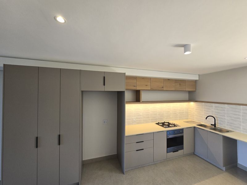 Modern kitchen featuring sleek grey cabinetry, wood-tone upper shelving, integrated gas hob, electric oven, and contemporary under-cabinet lighting in a clean, minimalist space.