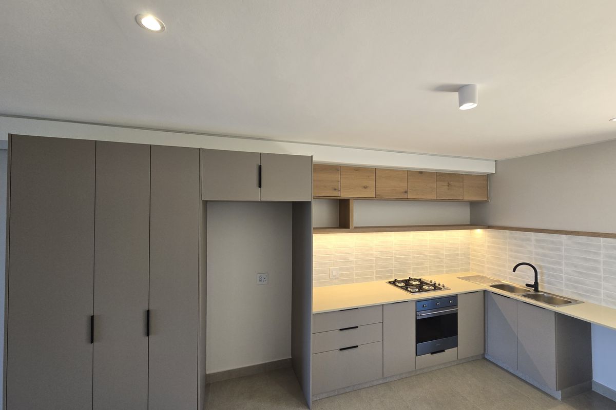 Modern kitchen featuring sleek grey cabinetry, wood-tone upper shelving, integrated gas hob, electric oven, and contemporary under-cabinet lighting in a clean, minimalist space.