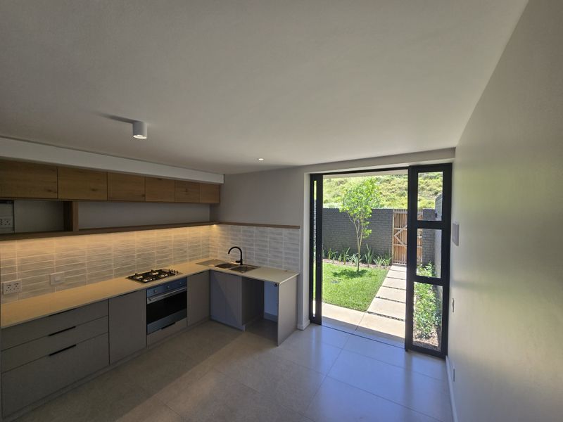 Modern open-plan kitchen featuring sleek cabinetry, integrated appliances, and seamless access to a private garden through a large sliding glass door.