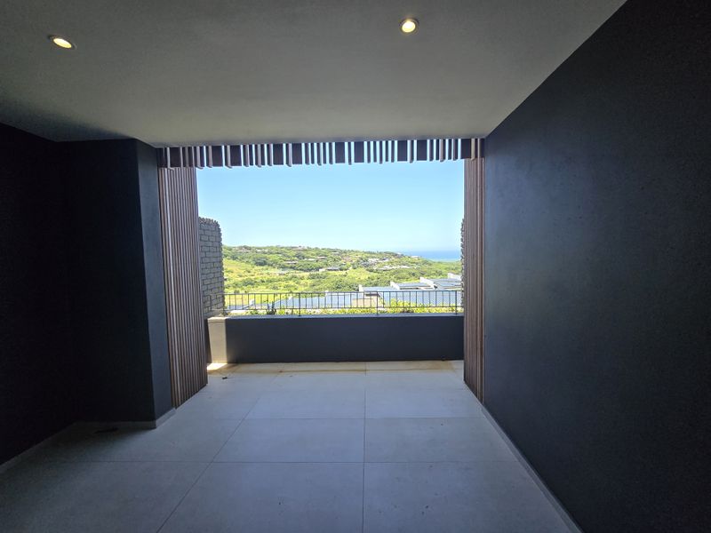 A modern, covered balcony featuring sleek tiled flooring, timber slat accents, and a metal balustrade, offering expansive views of the surrounding landscape.