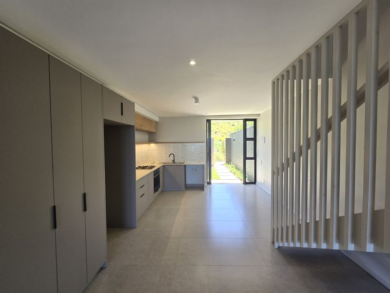 Modern open-plan kitchen and living area featuring sleek cabinetry, integrated appliances, tiled floors, and a stylish timber slat staircase screen leading to the outdoors.
