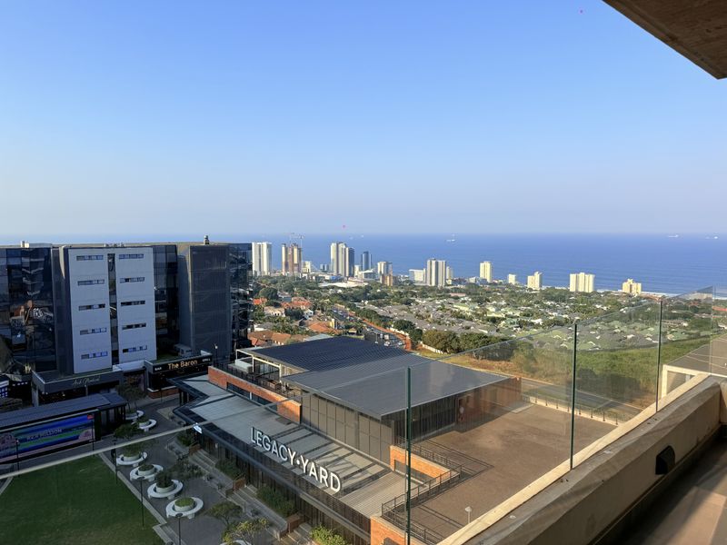 Elevated panoramic view overlooking the coastal urban landscape, ocean, and surrounding commercial developments from a modern balcony.