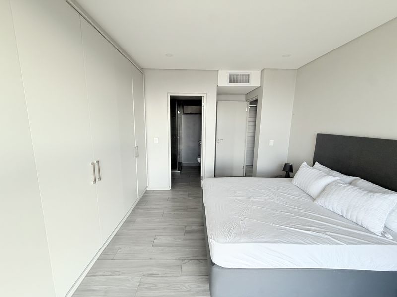 Modern bedroom featuring extensive built-in wardrobes, neutral tiled flooring, and integrated ducted air conditioning with direct access to an en-suite bathroom.
