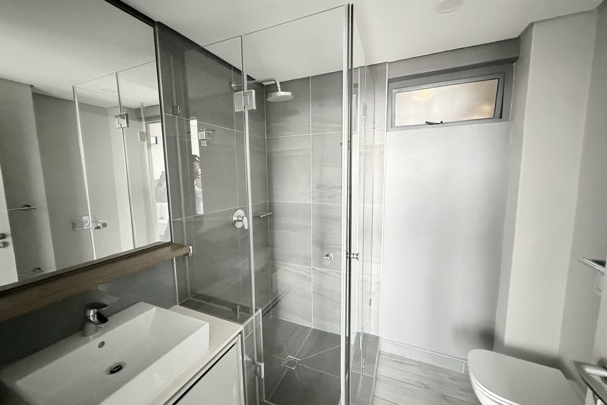 Modern bathroom featuring a glass-enclosed shower, vanity basin, wall-mounted mirror, and contemporary grey tiling throughout.