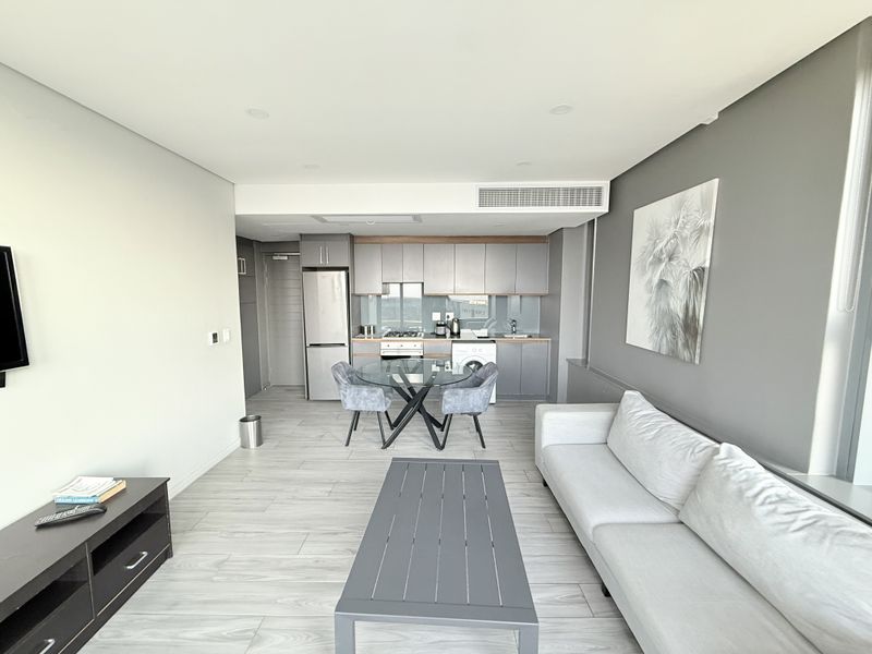 Modern open-plan living area featuring a sleek kitchen with built-in cabinetry, integrated appliances, and neutral tiled flooring throughout.